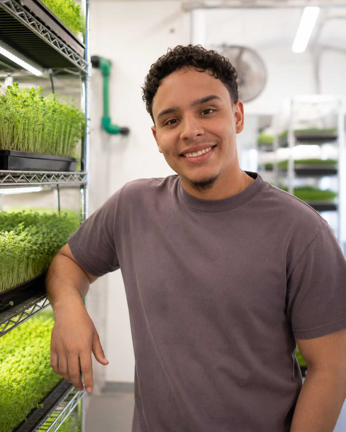 Santi smiling next to a tray rack of microgreens in the grow room